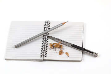 Note book with pencil and cutter on white background.