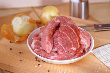 On a wooden Board plate of pork. Pork neck. Pieces of pork. Pork on a white plate. On the Board, onion, pepper, salt, knife. Studio light.