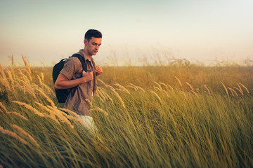 Handsome caucasian man with a backpack on his shoulders, time to go traveling. Tourism concept. Travel adventure of active sport man on a meadow.