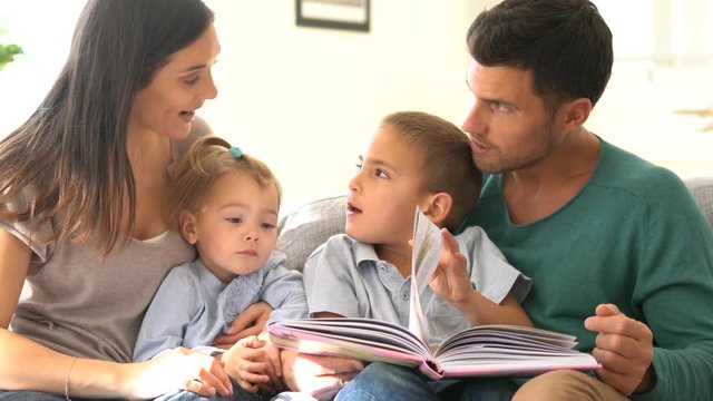 Family sitting on sofa reading book with kids