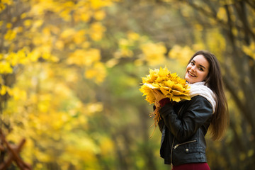 Young woman with autumn leaves in hand and fall yellow maple garden background