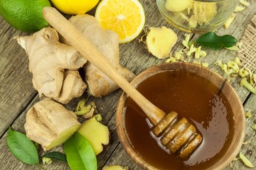 Preparing ginger tea against influenza. Traditional treatment for colds. Ginger, lemon and honey bowl on wooden table. Rustic wooden background. Home Pharmacy.
