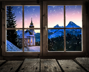 Blick aus dem Fenster einer Holzhütte auf eine Winterlandschaft mit kleiner Kirche - 127754394
