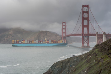 Cargo ship crossing the Golden Gate Bridge on a rainy day in springtime. Views seen from California Coastal Trail above Baker Beach. San Francisco, California, USA.