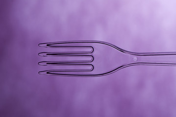 photo of plastic transparent fork on purple background