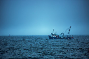 Trawler fishing boat sailing in open waters on a cold and foggy