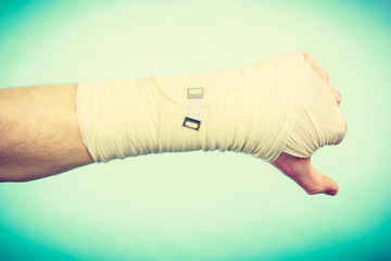 Male bandaged hand with thumb down sign.