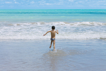 Six year old boy having fun on tropical beach in sunny day