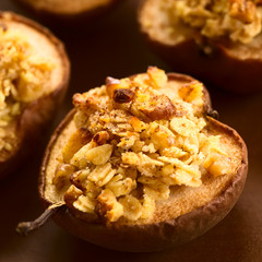 Gebackene Birnenhälfte mit einem Streusel aus Haferflocken, Walnuss und Zucker, bestreut mit Zimt, fotografiert mit natürlichem Licht (Selektiver Fokus, Fokus in die Mitte des Streusels auf der Birne)