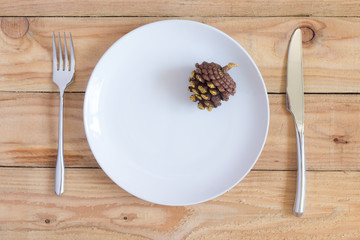 christmas dinner table : pine cone in white dish and silverware on wood table