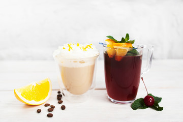 Latte and sangria glasses on white background. Two cups of coffee and punch with slice of orange, free space for advertisement or text. Refreshment, drink, party concept