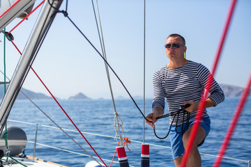 Young man skipper at his sail boat, controls ship during sea yacht race. Luxery vacations, sailing, adventure, travel.