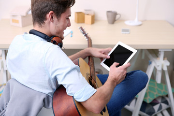 Young man with guitar and tablet sitting at table