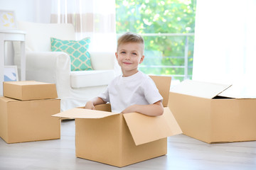 Little cute boy playing with cardboard boxes at home