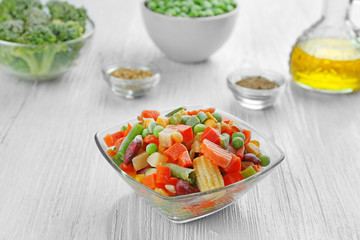 Frozen vegetables in bowl on wooden background