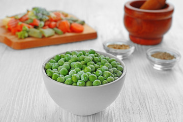 Frozen peas in bowl on wooden background