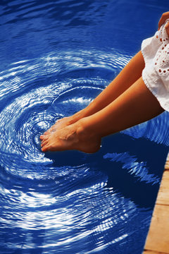 Relaxation. Young woman wets feet in water. (Sea, ocean, travel)