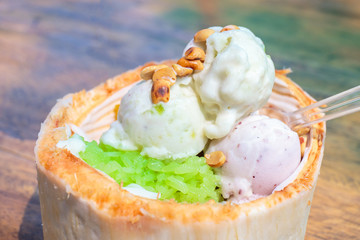 Ice cream made from coconut milk with nuts and sticky green rice in coconut shell on the wooden table.