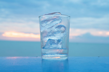 A glass with ice and sunset at sea with quiet feel or blue tone on the background