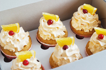 Vanilla cupcakes with a cap of cream on white wooden tablein the box