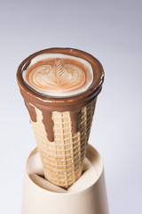 Coffee in waffle ice cream cone with latte art in the milk foam, isolated, close up