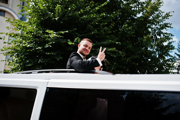 Groom shows two victory fingers from limousine car sunroof at we