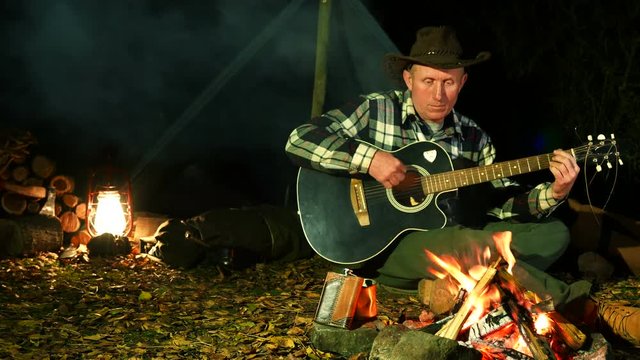 4K.Man   in cowboy hat  near  bonfire plays  guitar. Autumn travel life. 