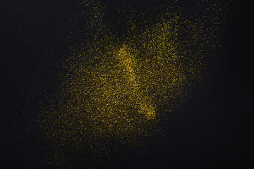 Golden glitter sand texture on black, abstract background.