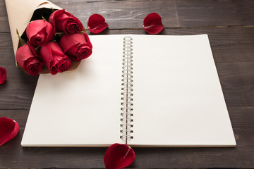 Red roses flower with the notebook are on the wooden background