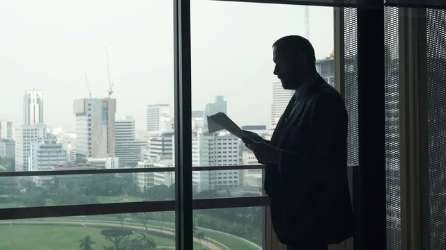 Young businessman reading and analyzing documents by window in office 
