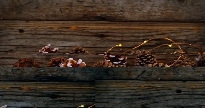 Pine cones with christmas lights on wooden plank