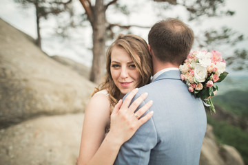 Gorgeous bride, groom kissing and hugging near the cliffs with stunning views