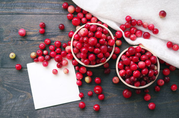 Fresh juicy cranberry  in wooden round bowls and white card with the inscription on a table, close up