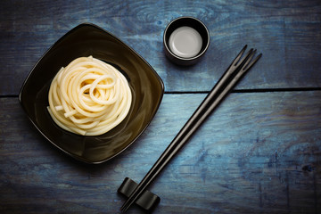 Spaghetti macaroni in black plate with chopsticks at wooden tabl