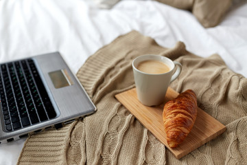 laptop, coffee and croissant on bed at cozy home