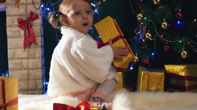 Girl opens Christmas gifts boxes near fireplace, decorated Cristmas tree