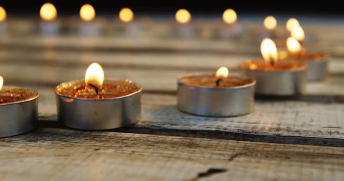 Close-up of burning candles kept in row on wooden plank