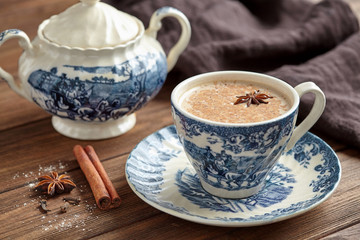 Masala tea chai latte homemade traditional hot Indian sweet milk with spices, herbs infusion healthy beverage in porcelain cup on wooden table background
