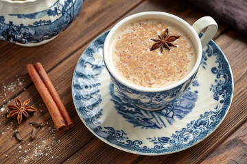 Masala tea chai latte traditional hot Indian teatime ceremony sweet milk with spices, herbs organic infusion healthy beverage in porcelain cup on wooden table background