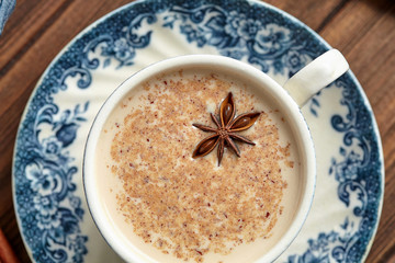 Masala tea chai latte traditional hot Indian sweet milk with spices, herbs blend organic infusion healthy beverage in porcelain cup on wooden table background