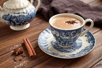 Masala tea chai latte traditional warm Indian sweet milk with spices, cinnamon stick, herbs blend organic infusion healthy beverage in porcelain cup on wooden table background
