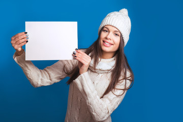 Love winter. Pretty young happy woman in winter clothes Woman surprise showing product .Beautiful girl with curly hair pointing to the side . Presenting your product