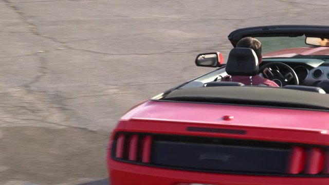 Man drifting stylish red cabriolet on empty parking lot at sunny day