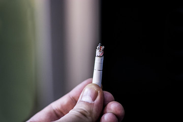 Color image of a male hand holding burning cigarette.