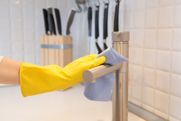 Close up of female hand in rubber yellow protective gloves cleaning the kitchen metal tap with a rag. Home, housekeeping concept