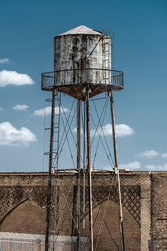 Old rusty water tower next to a brick wall blue sky sky utility infrastructure storage reservoir