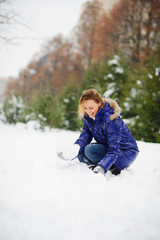 Fototapeta na wymiar Young woman in the winter park begins to build a snowman. I