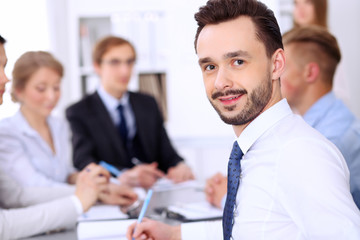 Portrait of cheerful smiling businessman  against a group of  people at meeting.