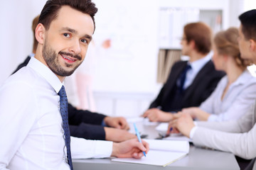 Portrait of cheerful smiling businessman  against a group of  people at meeting.