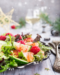 Fresh salad with smoked salmon, shrimps, raspberries and cherry tomatoes on white wooden background. Delicious Christmas themed dinner table